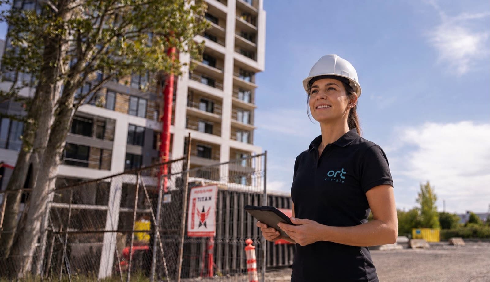 ORT Énergie engineer holding a tablet in front of a building under construction